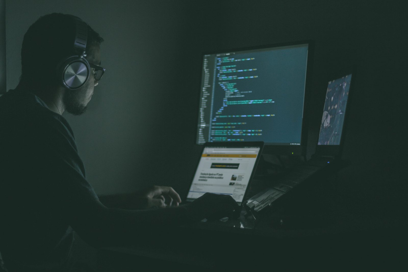 Person with headphones sits in front of three computer screens